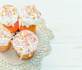 Happy Easter cake with sprinkles on glaze. Cake on light green rustic wooden board covered by lace cloth. Festive homemade bakery, spring holiday preparation. Selective focus, free text space.