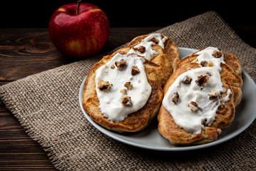 Apple pancakes with yogurt and walnut on dark wooden background.