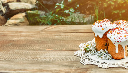 Happy Easter cake with sprinkles on white glaze. Cake on white rustic board, lace cloth, blur green plants and sun. Homemade bakery, spring holiday preparation. Selective focus, free text space.