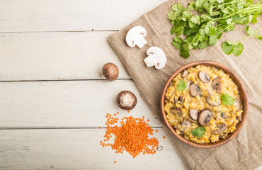 Lentils porridge with champignons. and coriander in a wooden bowl on a white wooden background. Top view, copy space.