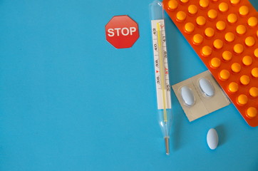 On a blue background a thermometer for measuring the temperature of a persons body, pills, tablets.