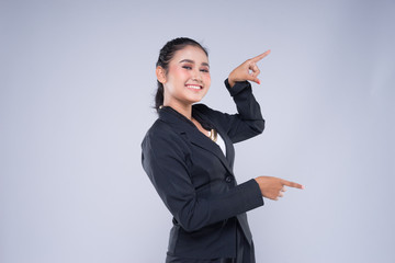 An attractive woman wearing business attire with gestures towards copyspace area isolated on grey....