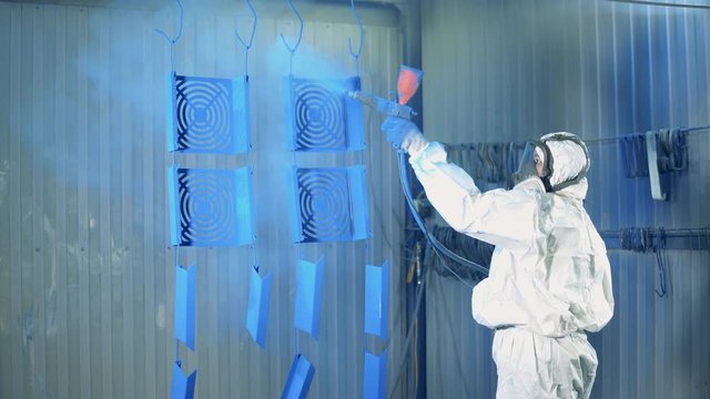 Blue paint is getting sprayed onto metal plates by a female worker. Industrial painting process at painting factory facility.