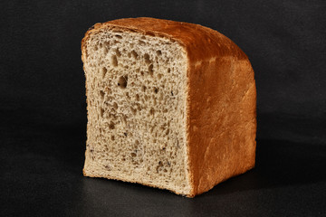 Half a loaf of fresh, delicious baked gray bread against black background with copy space. Close-up, side view