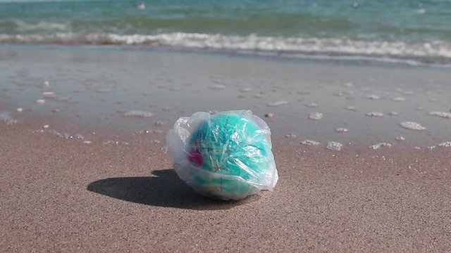 Globe ball in a plastic bag on the beach near the sea. Ecological catastrophe concept