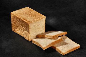 Sliced loaf of fresh, palatable baked white bread against black background with copy space. Close-up