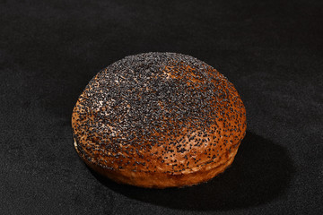 Fresh, delicious baked bun sprinkled with poppy seeds against black background with copy space. Rural cuisine or bakery. Close-up