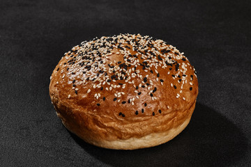 Fresh, tasty baked bun sprinkled with sesame seeds against black background with copy space. Rural cuisine or bakery. Close-up