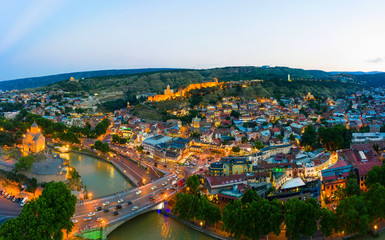 The evening panorama of the old town in the old district of Avlabari, Virgin Mary Metekhi church and Rike Park, the Kura river reflects the evening city lights in Tbilisi, Georgia. © miklyxa