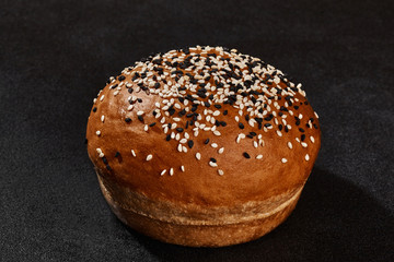 Fresh, delicious baked bun sprinkled with sesame seeds against black background with copy space. Rural cuisine or bakery. Close-up