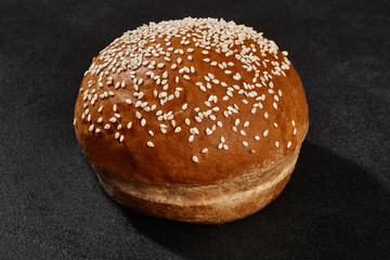 Fresh, yummy baked bun sprinkled with sesame seeds against black background with copy space. Rural cuisine or bakery. Close-up
