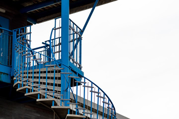 Blue and grey painted metal spiral outdoor staircase with metal railing set against contrasting...