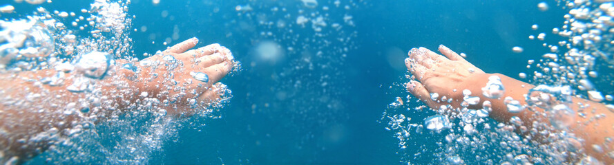 Underwater shoot of a diver swimming in a blue clear water, strong hands and lots of bubbles. Point of view shot
