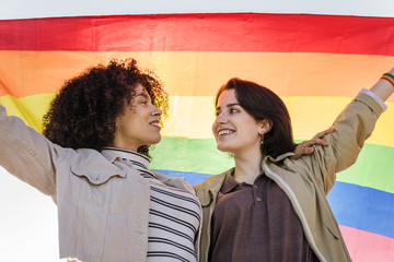 young lesbian couple embrace under a rainbow flag