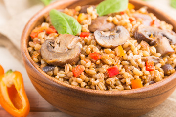 Spelt (dinkel wheat) porridge with vegetables and mushrooms in wooden bowl on a white wooden background and linen textile. Side view, selective focus.