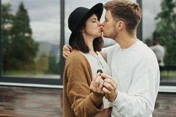 Stylish hipster couple holding together key from their new home on background of terrace and big...