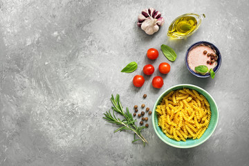 Obraz na płótnie Canvas Raw pasta and ingredients for cooking. Fusilli, tomatoes, basil, olive oil, pink salt, pepper, rosemary and garlic on a gray concrete background. Top view, copy space