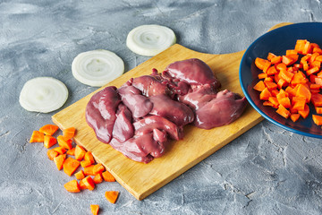 raw fresh liver on a plate with chopped vegetables onions and carrots. gray background
