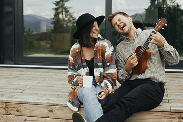 Happy young family travelers smiling and having fun. Hipster man playing on ukulele for his stylish...