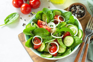 Diet menu. Healthy vegetable salad of fresh tomato, cucumber, onion and spinach on slate, stone or concrete background. Copy space.