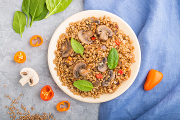 Spelt (dinkel wheat) porridge with vegetables and mushrooms on ceramic plate on a gray concrete background. Top view, close up.