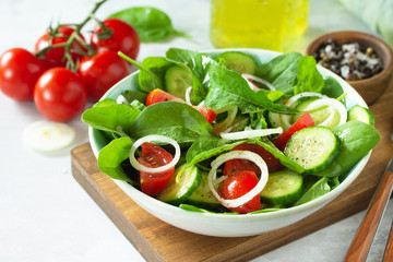Diet menu. Healthy vegetable salad of fresh tomato, cucumber, onion and spinach on slate, stone or concrete background. Copy space.