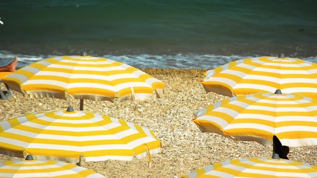 Yellow and white striped umbrellas open in a pebbly beach during a windy summer day