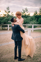 Young bridegroom holds in his arms his beautiful bride on a ranch, full-length portrait