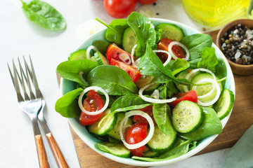 Diet menu. Healthy vegetable salad of fresh tomato, cucumber, onion and spinach on slate, stone or concrete background.
