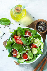 Diet menu. Healthy vegetable salad of fresh tomato, cucumber, onion and spinach on slate, stone or concrete background. Top view flat lay background.