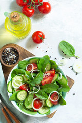 Diet menu. Healthy vegetable salad of fresh tomato, cucumber, onion and spinach on slate, stone or concrete background. Top view flat lay background. Copy space.