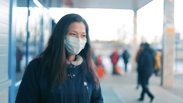 Sick girl with Chinese coronavirus in a public place. Wearing a protective mask prevents infection of other people. The woman has chills and fever, symptoms of infection.