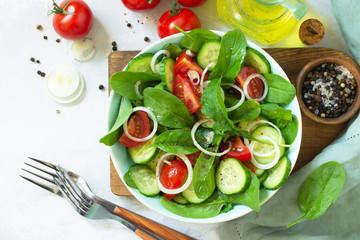 Diet menu. Healthy vegetable salad of fresh tomato, cucumber, onion and spinach on slate, stone or concrete background. Top view flat lay background.