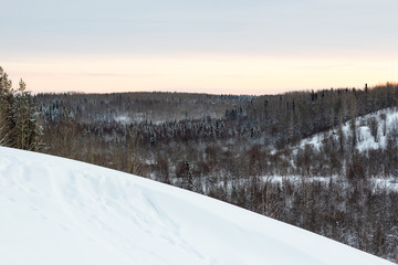 Fototapeta na wymiar winter snow landscape: a snow hill with a beautiful view of the winter forest and the sunset sky