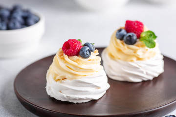 Delicious Pavlova cake with whipped cream and fresh berries on wooden plate. Selective focus