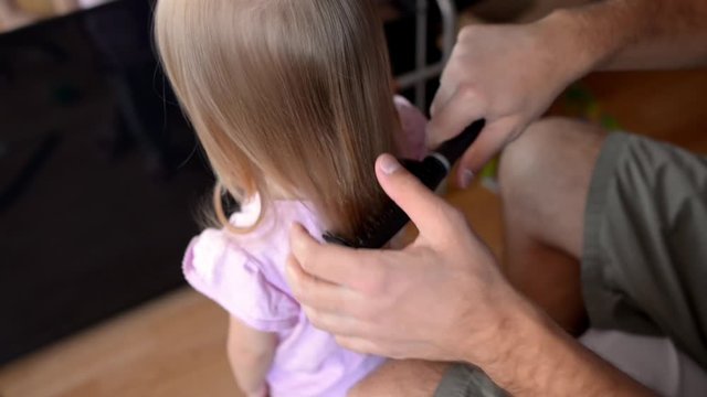 Father combing knots in his daughter hair calmly standing in front of him