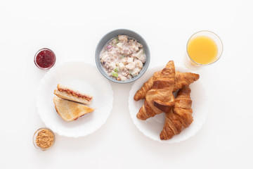 Tasty and healthy breakfast. Croissants, orange juice, a sandwich with jam and peanut butter, granola with yogurt, banana and apple