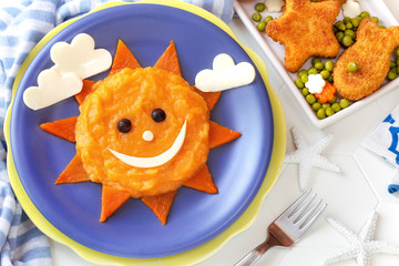 Fun food for kids - cute smiling sun face made of mashed potato and pumpkin puree, decorated with...