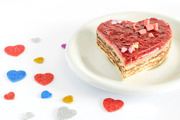 For Valentines day sweet cake in a form of heart on the white plate and on the white background with some little colorful hearts.