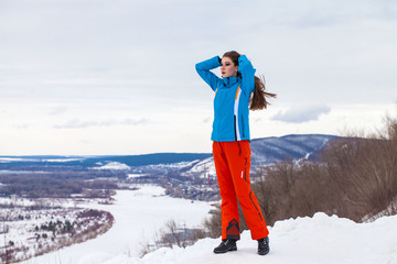 Young brunette woman in a ski suit posing on a hilltop