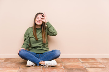 Young caucasian woman sitting on the floor isolated excited keeping ok gesture on eye.