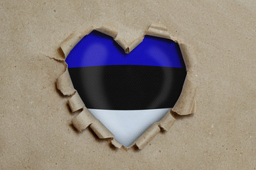 Heart shaped hole torn through paper, showing Estonian flag
