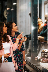 Two happy young women with shopping bags having fun and pointing finger in the shop window.
