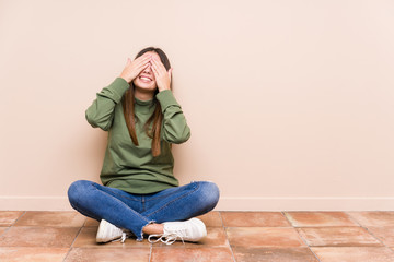 Young caucasian woman sitting on the floor isolated covers eyes with hands, smiles broadly waiting for a surprise.