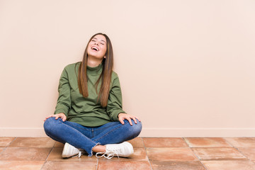 Young caucasian woman sitting on the floor isolated relaxed and happy laughing, neck stretched showing teeth.