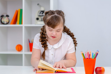 A girl with down syndrome is sitting at home and reading a book.