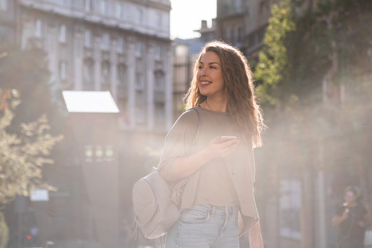 Front view portrait of a cute young woman holding mobile phone and looking away