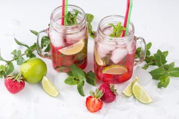 Cold lemonade with strawberries, mint and lime. On a white background, decorated with strawberries, lime, mint and ice.