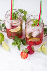 Cold lemonade with strawberries, mint and lime. On a white background, decorated with strawberries, lime, mint and ice.