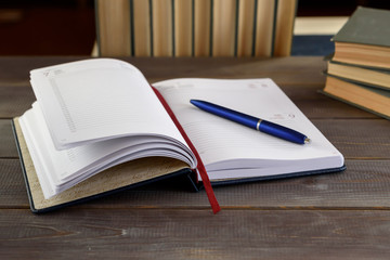 Open note book with pen and books on a wooden table. University exam preparation concept.